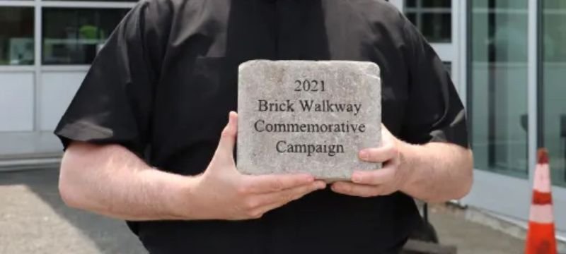 Fr. Dolan holding a commemorative brick sample