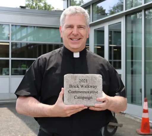 Fr. Dolan holding a commemorative brick sample